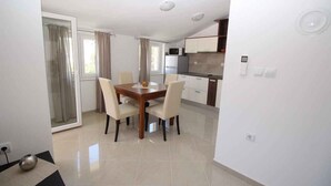 A modern kitchen with a dining area, featuring a wooden table and chairs, a microwave, and a refrigerator. - Holiday apartment with shared-use pool (Baška)