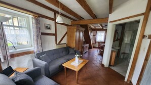 Ein gemütliches Wohnzimmer mit einer grauen Couch, einem Holztisch und Blick auf eine Küche und Essecke durch einen offenen Durchgang.