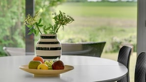 A round table with a white surface, a wooden bowl with fruits, and a striped vase with flowers. - Amazing home in Bogense with WiFi (Bogense)