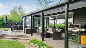 Une terrasse extérieure couverte, équipée d’un barbecue, d’un espace salon et offrant une vue sur le paysage environnant.