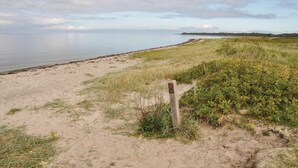 A sandy beach with a wooden post and a sign, leading to a calm body of water. - Amazing home in Bogense with WiFi (Bogense)