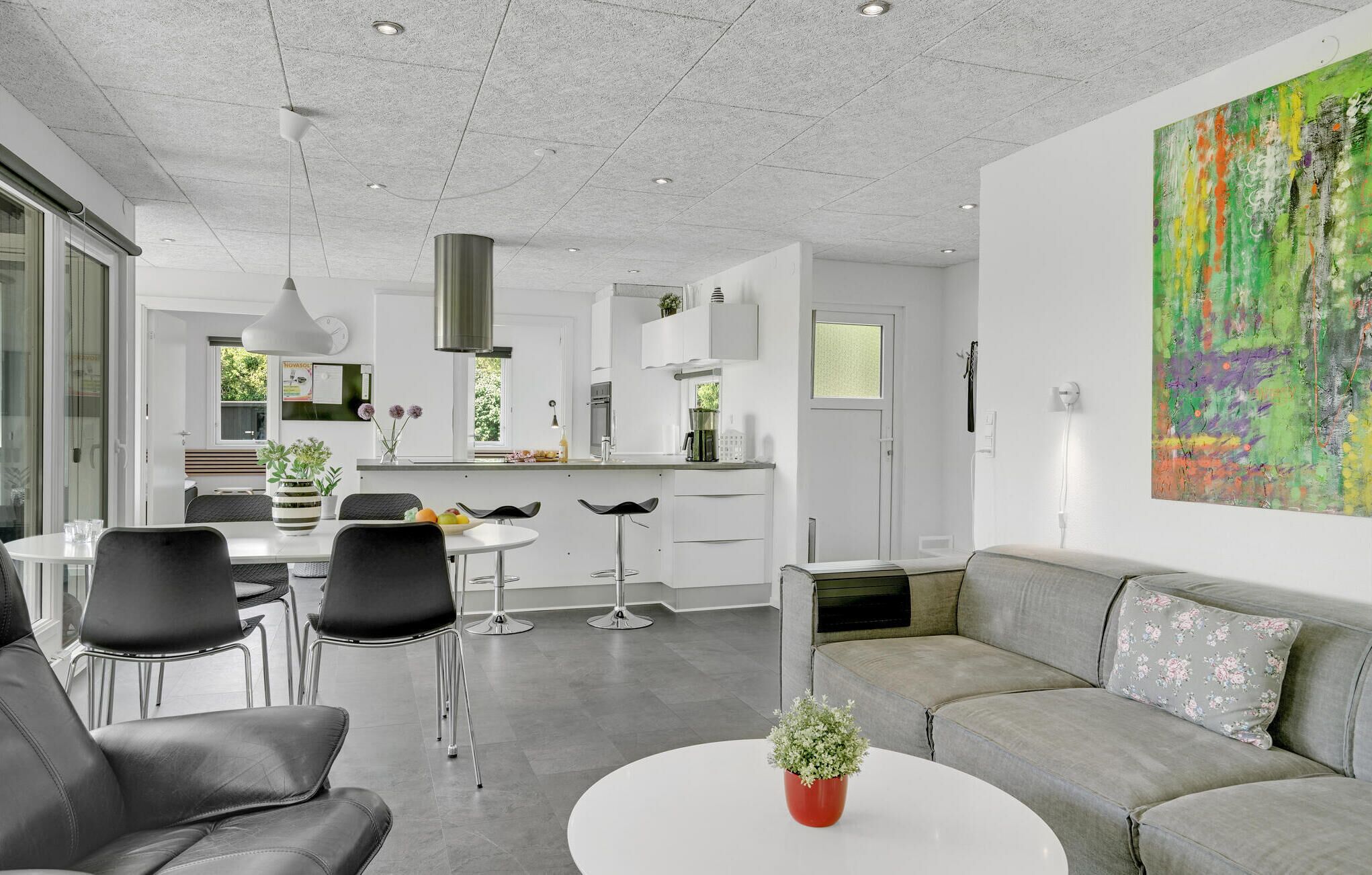Une cuisine moderne avec des armoires blanches, une hotte en acier inoxydable et un coin repas comprenant une table blanche et des chaises noires.