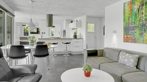 A modern kitchen with white cabinets, a stainless steel range hood, and a dining area with a white table and black chairs. - Amazing home in Bogense with WiFi (Bogense)