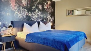 Een slaapkamer met een bed, nachtkastje en een bloemen behang.