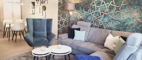 A modern living room with a grey sofa, a blue armchair, and a small round table with two candles.