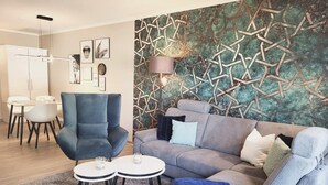 Een moderne woonkamer met een grijze bank, een blauwe fauteuil en een kleine ronde tafel met twee kaarsen.