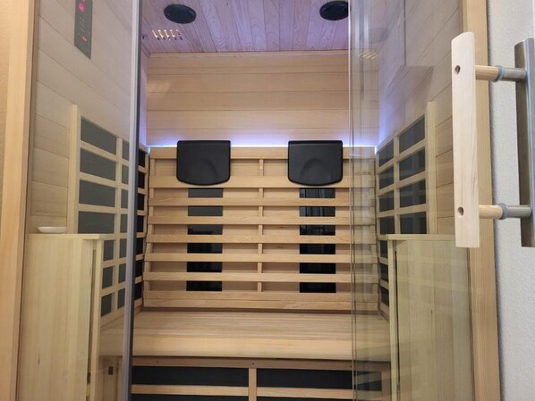 Un sauna doté de bancs en bois et de portes en verre, équipé de haut-parleurs et d’un panneau de commande.