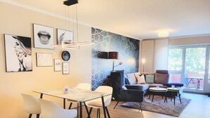 Een moderne woonkamer met een eethoek, met een bank, stoelen, een salontafel en kunst aan de muren.