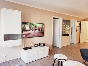 Ein modernes Wohnzimmer mit Flachbildfernseher, einem weißen Schrank, einem kleinen runden Tisch und einem schwarzen Sessel.
