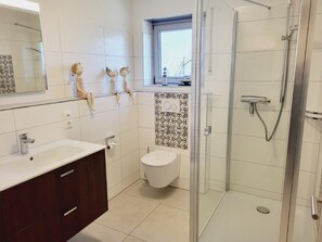 A modern bathroom with a glass-enclosed shower, a white sink, and a toilet.