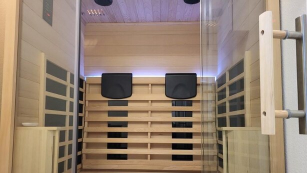 Een sauna met houten banken en glazen deuren, voorzien van speakers en een bedieningspaneel.