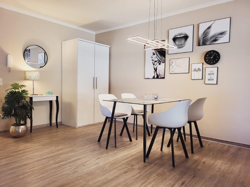 A modern dining area with a white table, four chairs, and a hanging light fixture.