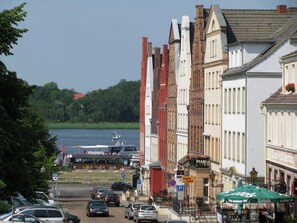 A street view with buildings, parked cars, and a body of water in the background. - Haferland Vacation Rental (2) - Small Guesthouse (Rostock)