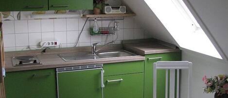 Una cocina con armarios verdes, un lavabo blanco y una radio sobre una estantería.