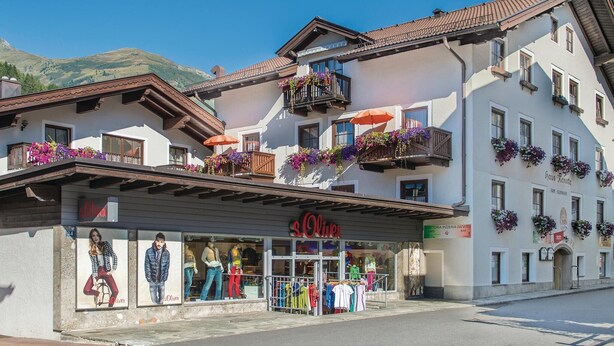 Ein Hotel mit Balkonen, die mit Blumen geschmückt sind, ein sichtbarer Laden mit Schaufensterpuppen und ein Schild mit der Aufschrift "S. Oliver".