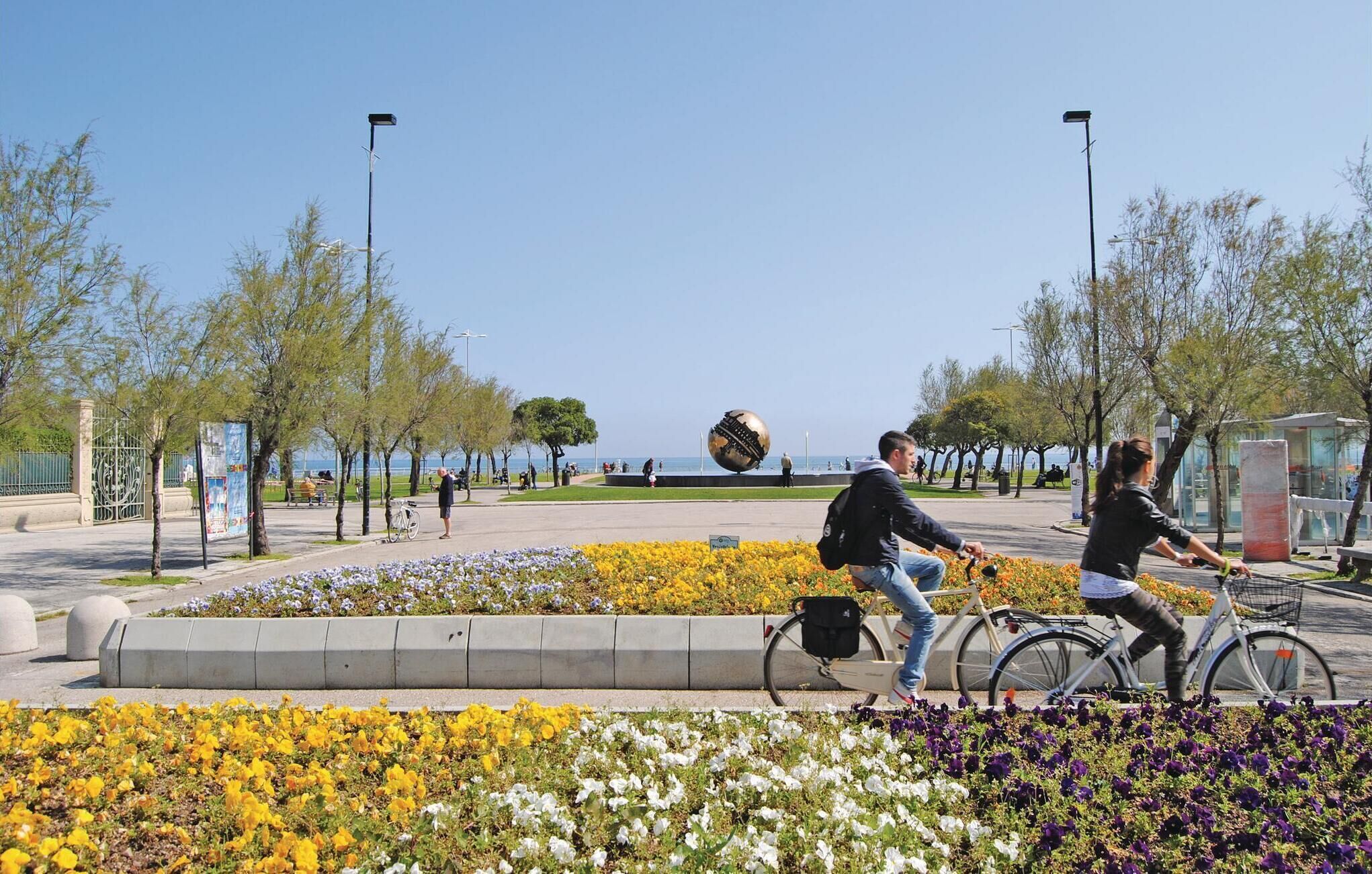 Een park met bloemperken, een groot metalen sculptuur en een waterpartij in de achtergrond.