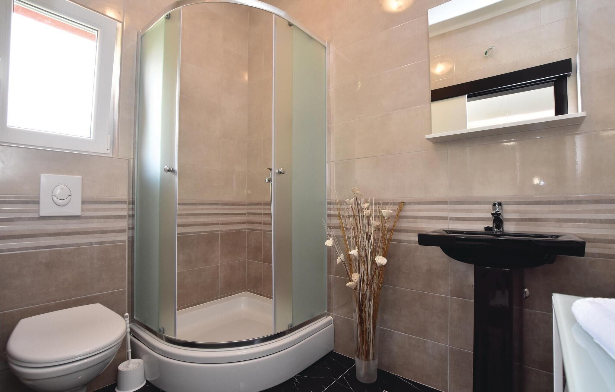Un baño con ducha acristalada, inodoro, lavamanos y un jarrón decorativo con cañas.