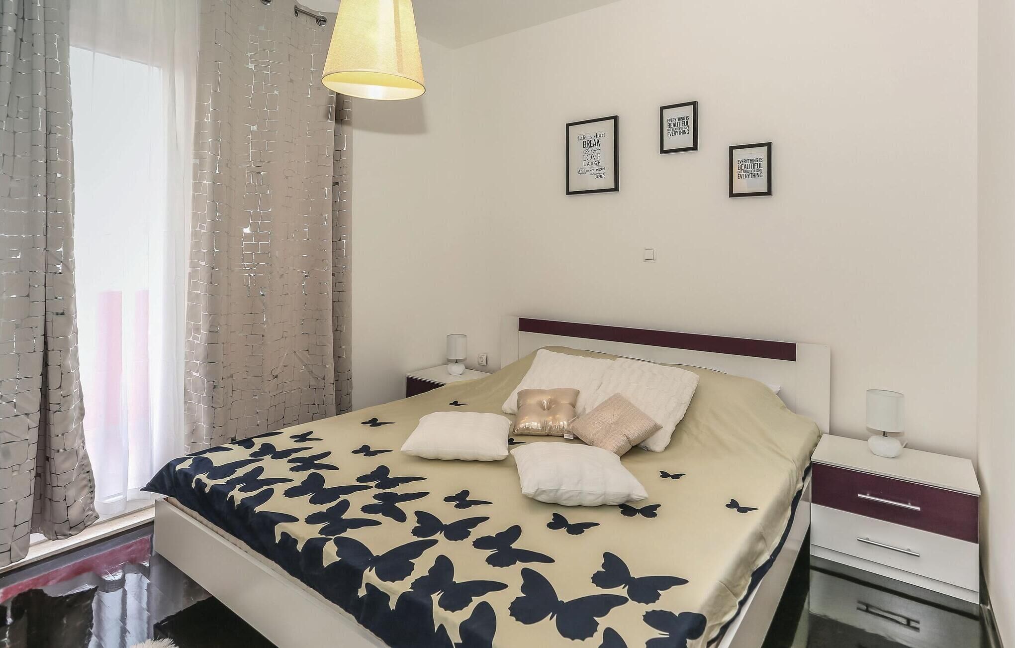 Ein ordentlich bezogenes Bett mit einem gemusterten Bettdeckenüberwurf, zwei Nachttischlampen, einem Nachttisch und zwei gerahmten inspirierenden Zitaten an der Wand.