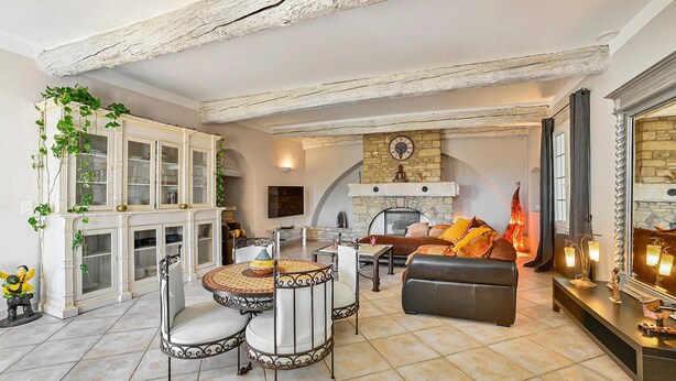 A living room with a fireplace, a dining area with a round table and chairs, and a sofa with cushions.
