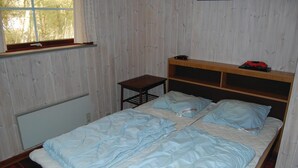 A bedroom with a wooden headboard, a bed with a blue duvet, a small table, and a window with curtains. - Amazing home in Rømø with kitchen (Rømø)