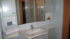 A bathroom with a sink, mirror, and a small shelf with toiletries. - Double room - online - Gästezimmer Wolter (Lutherstadt Wittenberg)