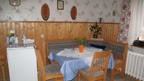 A dining area with a wooden table and chairs, a small refrigerator, and a clock on the wall. - Double room - online - Gästezimmer Wolter (Lutherstadt Wittenberg)