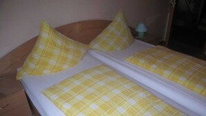 A bed with yellow checkered bedding and pillows, a wooden headboard, and a nightstand with a lamp. - Double room - online - Gästezimmer Wolter (Lutherstadt Wittenberg)