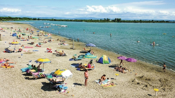 A beach with numerous umbrellas and sun loungers, a calm sea, and boats in the distance. - Beautiful home in Belvedere di Aquileia with WiFi (Belvedere di Aquileia)