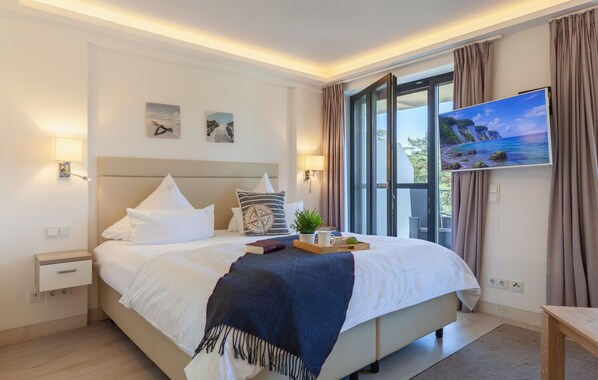 Una habitación de hotel moderna con una cama grande, un televisor y un ventanal con cortinas.