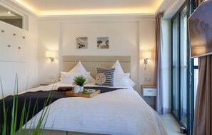 Una habitación de hotel con cama, mesitas de noche, ventana y cuadros en la pared.