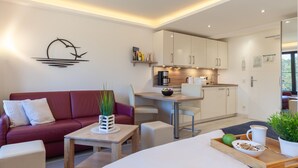 A modern living room with a red sofa, a wooden coffee table, and a dining area with a kitchen in the background. - Lovely apartment in Binz with WiFi (Prora/Rügen)