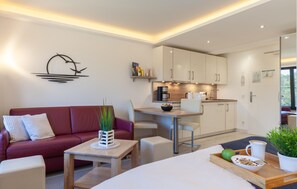 Una sala de estar moderna con un sofá rojo, una mesa de centro de madera y un comedor con una cocina al fondo.