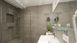 A modern bathroom with a glass shower enclosure, a white sink, and a glass shelf with toiletries. - Lovely apartment in Binz with WiFi (Prora/Rügen)