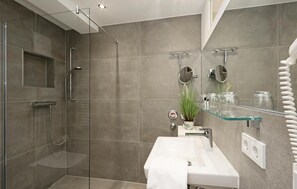 Un baño moderno con cabina de ducha de vidrio, un lavabo blanco y una repisa de vidrio con artículos de aseo.