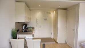 A compact kitchen with white cabinets, a dining table with chairs, and a small coffee machine. - Lovely apartment in Binz with WiFi (Prora/Rügen)