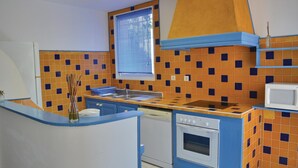 Une cuisine compacte avec des meubles bleus, une cuisinière blanche et un micro-ondes posé sur une étagère.