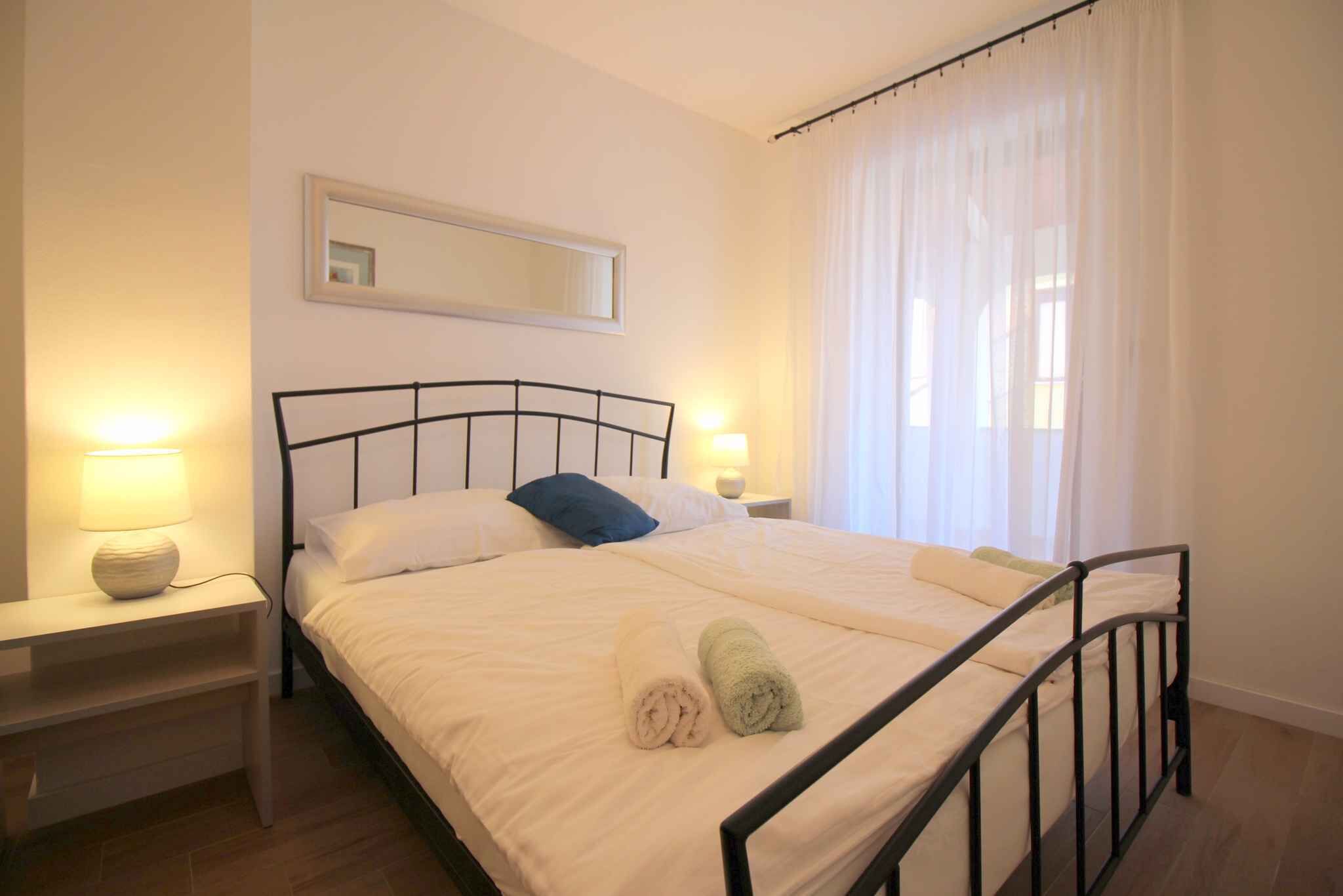 A neatly made bed with two rolled towels, a bedside lamp, and a nightstand.
