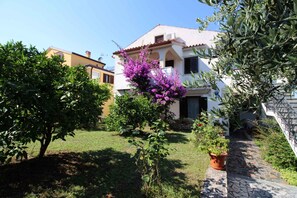 A residential property with a garden, a stone pathway, and a white building with a tiled roof. - Holiday apartment with balcony (Poreč)