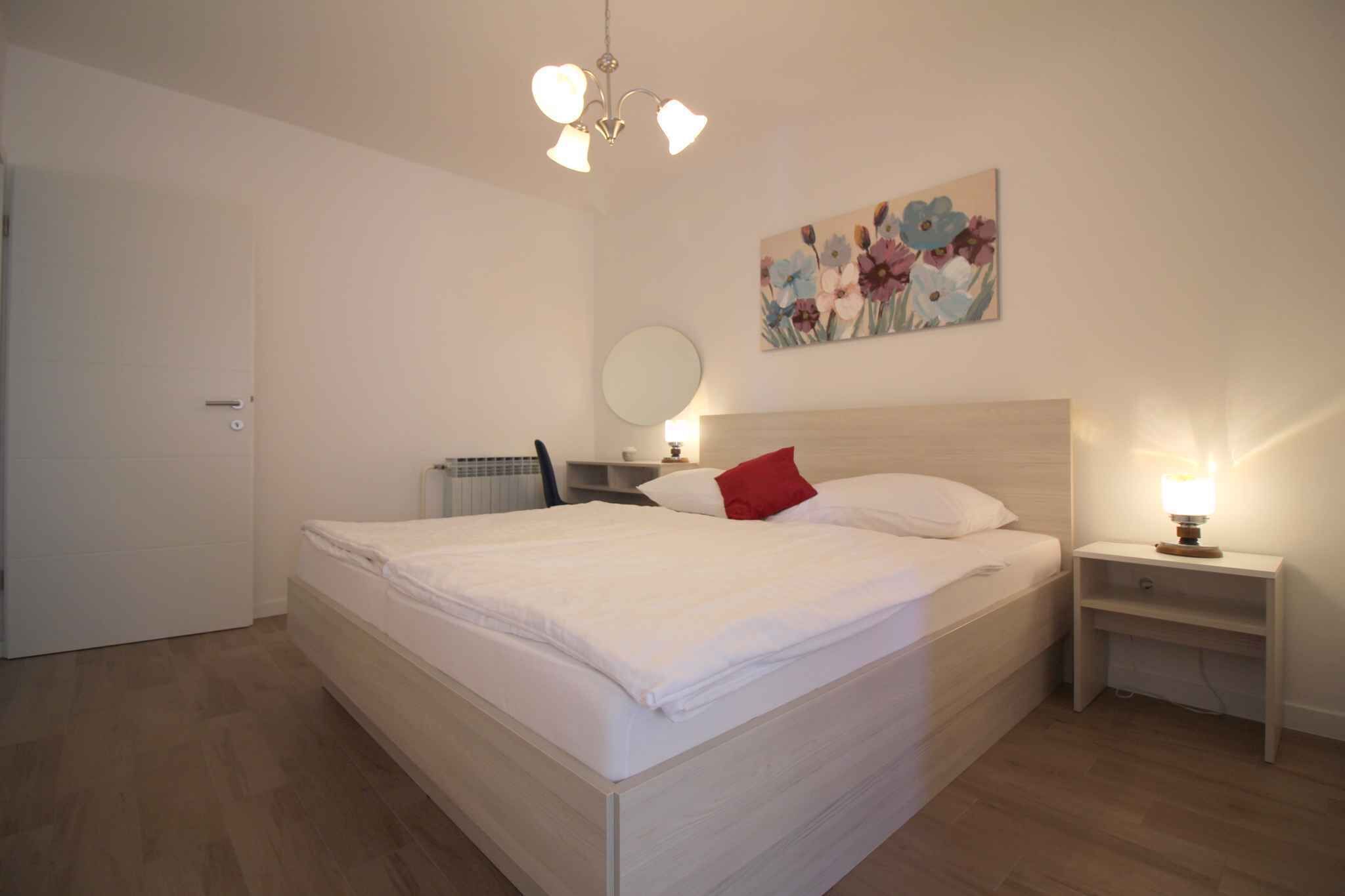 Un dormitorio con una cama grande, una mesita de noche con lámpara, un espejo en la pared y un cuadro con motivos florales.