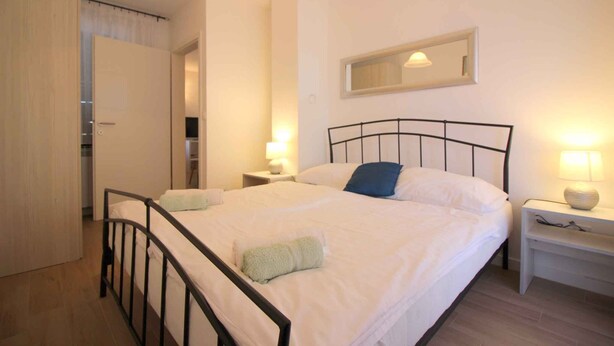 A neatly arranged bedroom with a bed, bedside tables, a mirror, and a door leading to a bathroom. - Holiday apartment with balcony (Poreč)