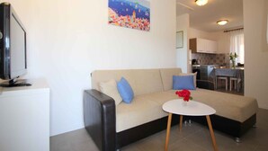 A living room with a sofa, a small round table, and a painting on the wall. - Holiday apartment with balcony (Poreč)