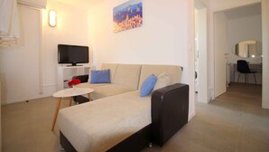 A modern living room with a sofa, a small round table with a vase of flowers, a flat-screen TV, and a painting on the wall. - Holiday apartment with balcony (Poreč)