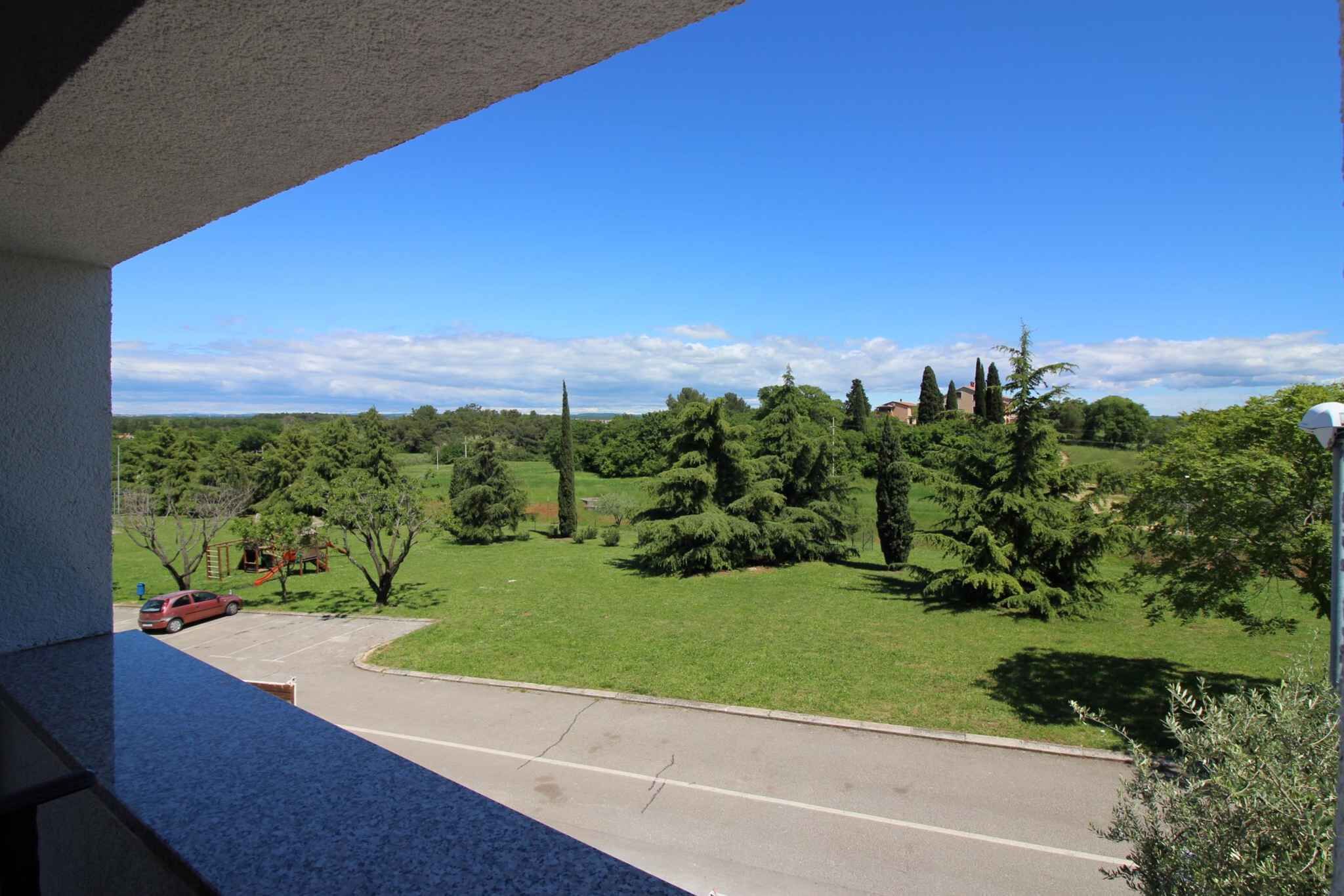 A balcony with a view of a green landscape, a road, and a parked car.