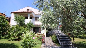 A two-story house with a tiled roof, a balcony, and a garden with various plants and flowers. - Holiday apartment with balcony (Poreč)