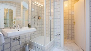 A modern bathroom with a glass shower enclosure, a white sink with a mirror, and a tiled floor. - Junior Suite for single use - Bio Design Boutique Hotel Landhaus St. Georg (Bad Wiessee)