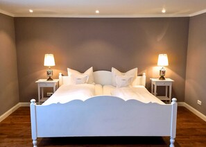 Un dormitorio con cama blanca, dos mesitas de noche con lámparas y pared gris.