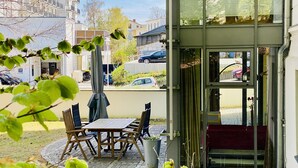 An outdoor seating area with a table and chairs, a trash bin, and a building entrance with a glass door.