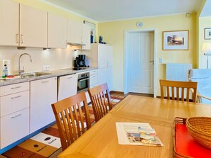 A compact kitchen with a dining area, including cabinets, a sink, a stove, and a dining table with chairs. - Villa Theresa 1 - Villa Theresa, App. 1 (Heringsdorf)
