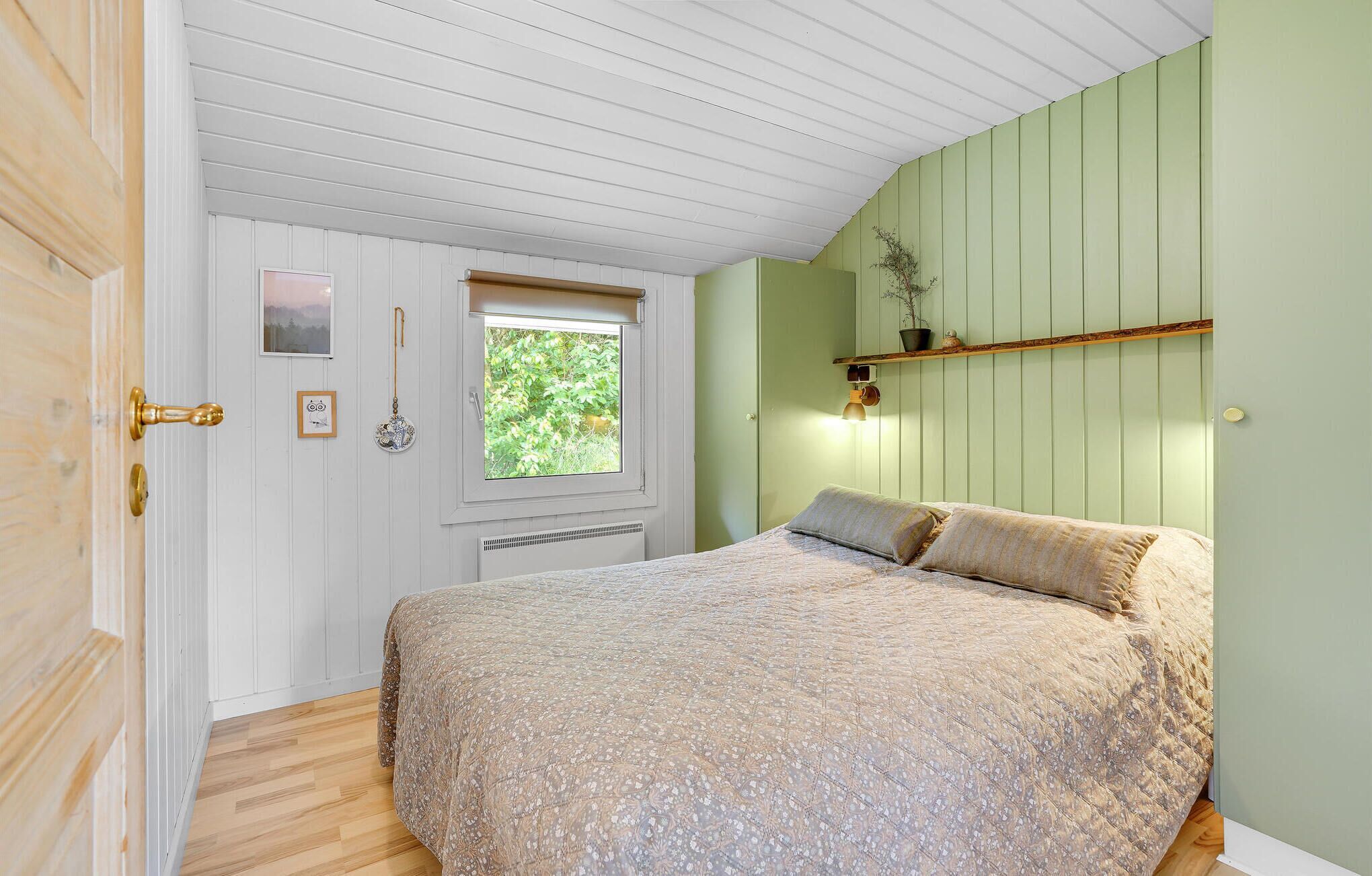 Un dormitorio con cama, ventana, puerta y repisa de pared con una planta.