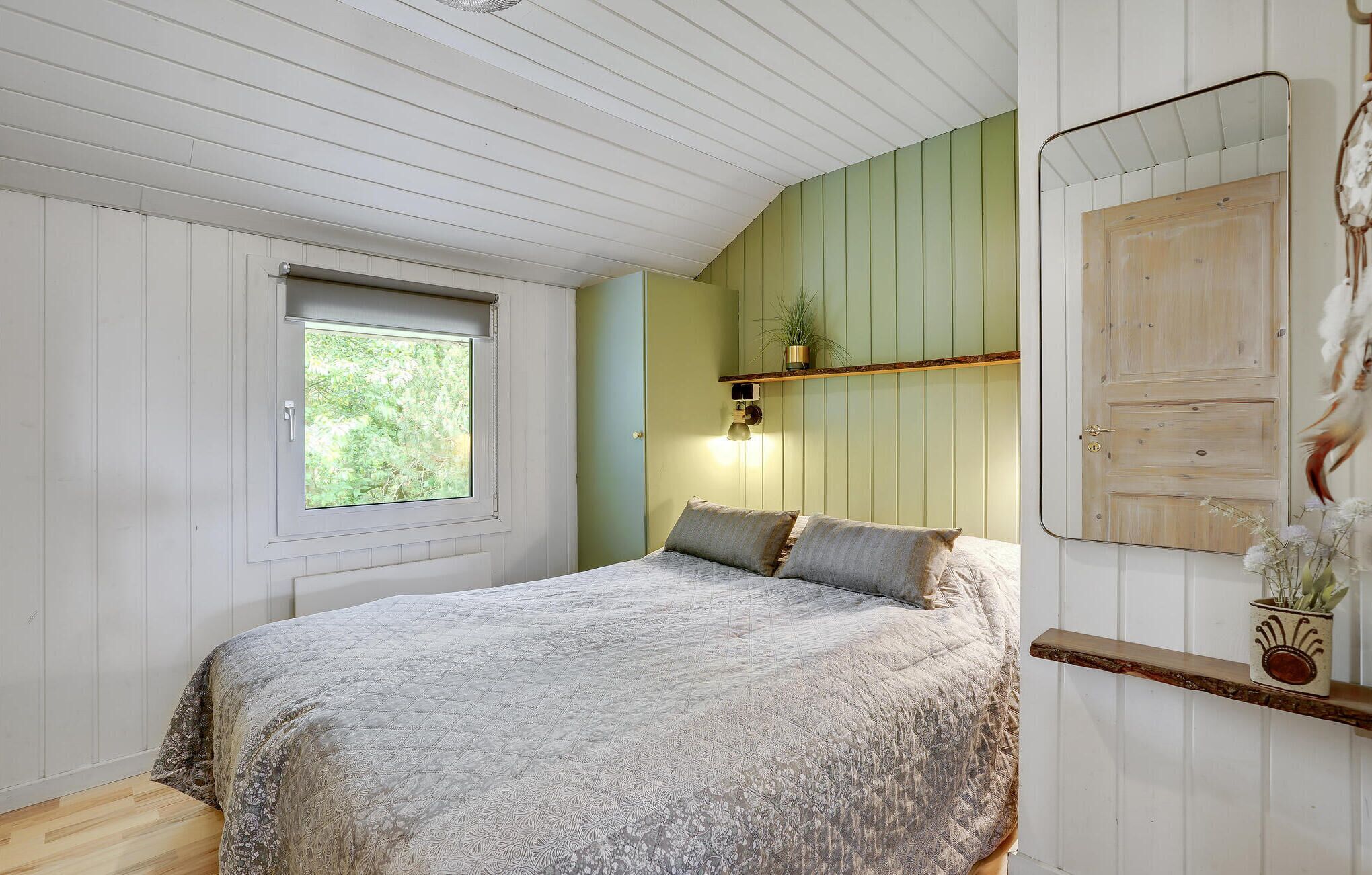 Une chambre à coucher avec un lit, une fenêtre, une lampe fixée au mur et une porte.